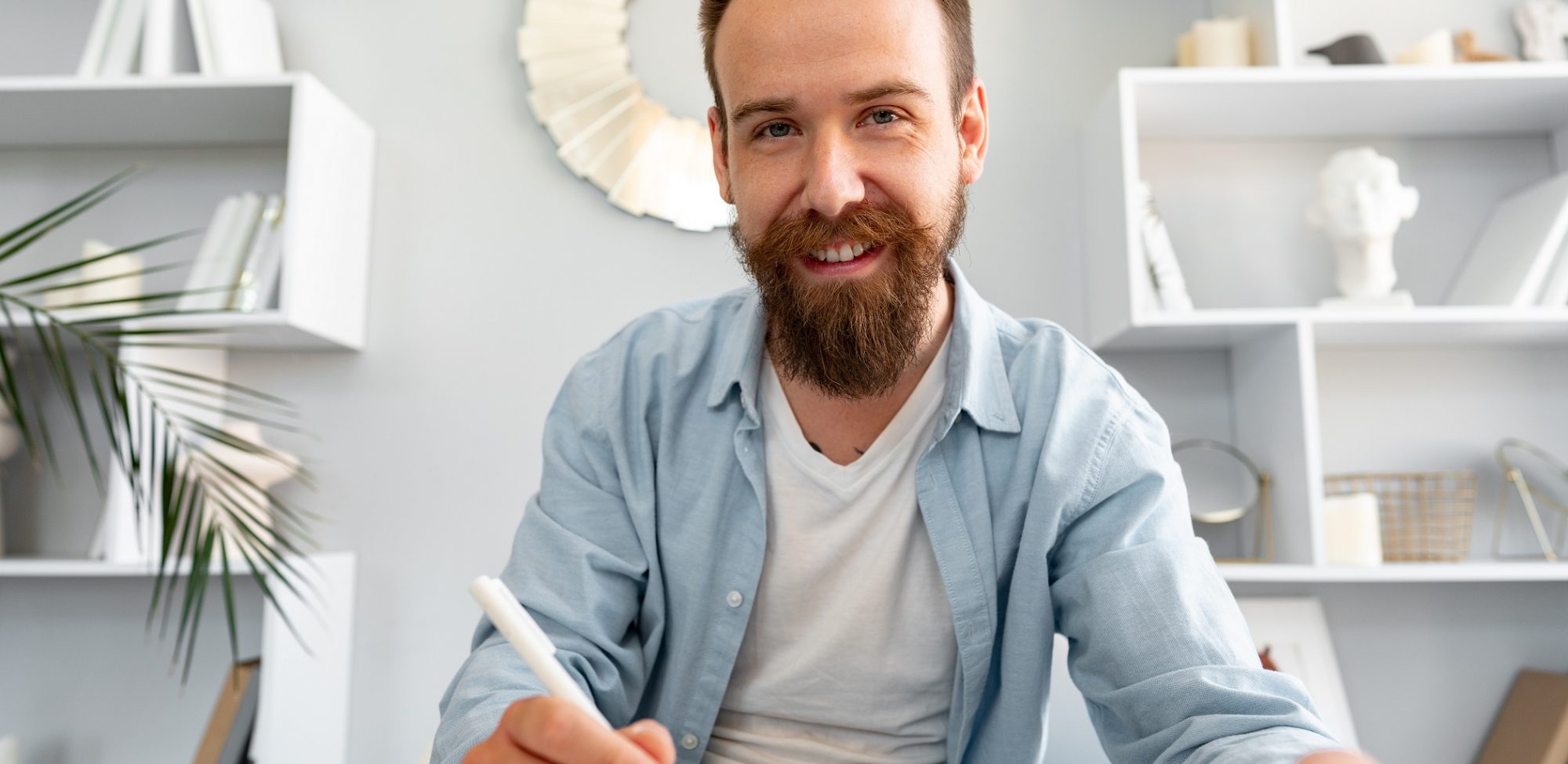 young bearded man sitting at the desk and taking notes at home
